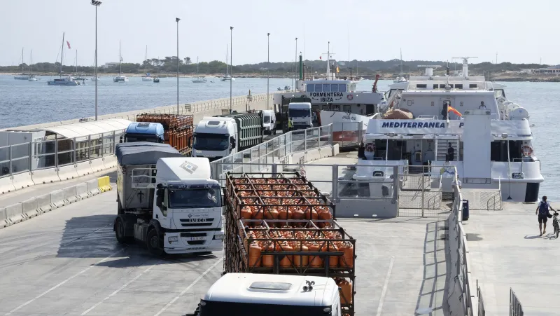 Muelle del puerto de La Savina con camiones de transporte de mercancías, incluidos vehículos que trasladan bombonas de gas y contenedores. Al fondo, ferries interinsulares atracados
